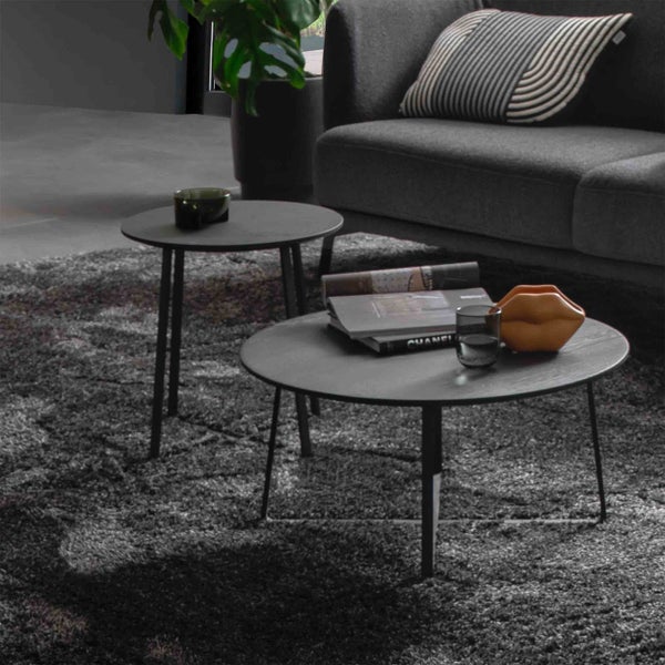 Zwei runde Couchtische aus schwarzem Metall und Holz in einem modernen Wohnzimmer auf einem grauen Teppich.