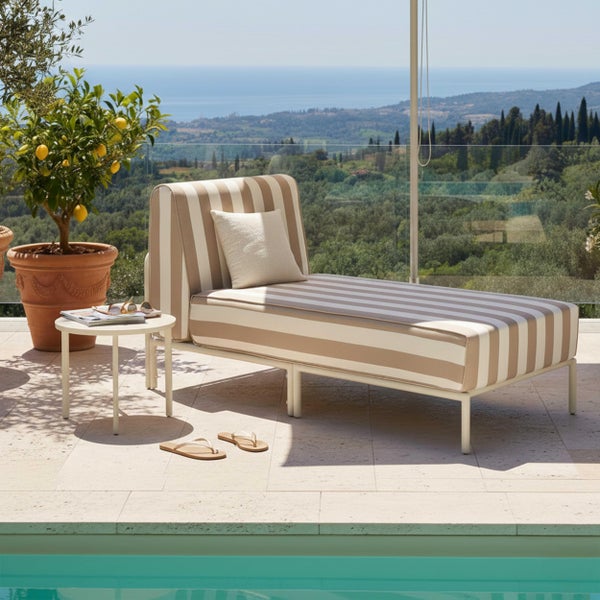 Gestreifte Gartenliege und runder Beistelltisch auf einer hellen Steinterrasse am Pool mit weitem Blick auf die Landschaft.