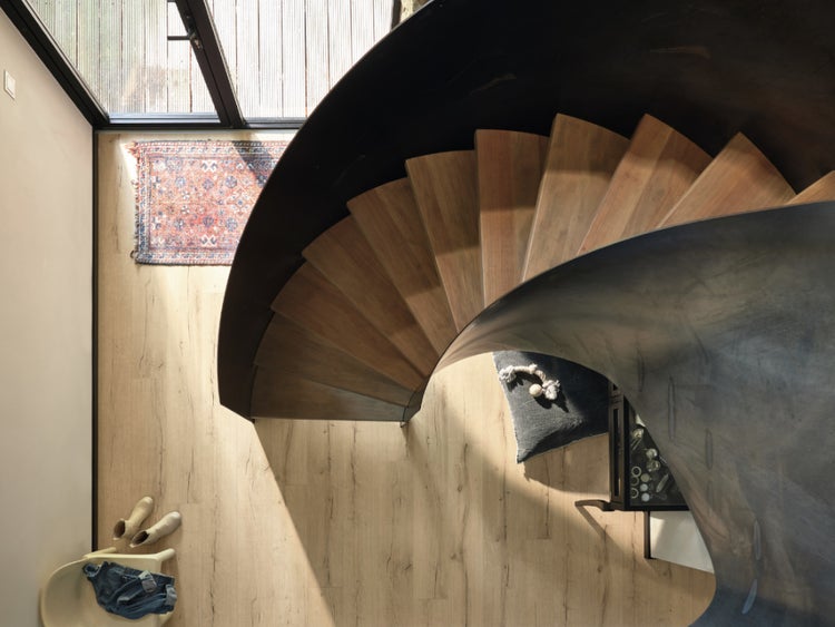 Draufsicht einer modernen Wendeltreppe aus Holzstufen mit schwarzem Metallgeländer in einem hellen Wohnraum mit Holzboden.