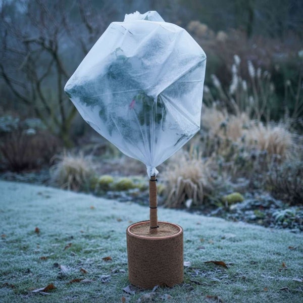 Winterschutzhaube aus Vlies über einer Pflanze mit Kokosmatte als Topfschutz im Garten
