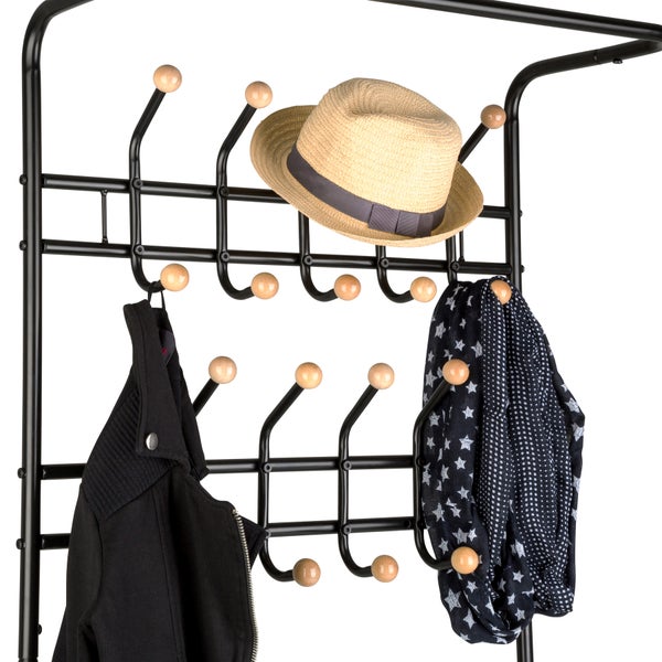 Schwarze Metall-Garderobe mit Holzkugeln an den Haken, bestückt mit einem Strohhut, einer schwarzen Jacke und einem gemusterten Schal.