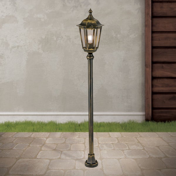 Klassische Außen-Wegeleuchte im Laternen-Design, antik-goldfarben, auf Pflastersteinen vor einer Gartenmauer.