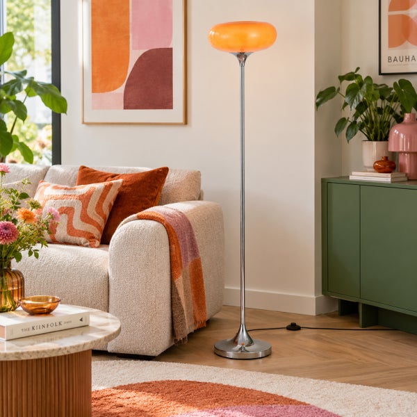 Moderne Stehleuchte mit flachem Glasschirm und schlankem Metallfuß im hell eingerichteten Wohnzimmer neben einem Sofa.
