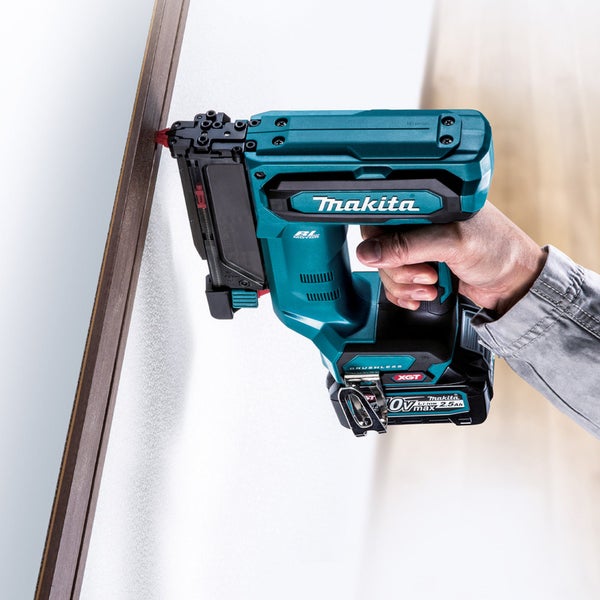 Eine Hand hält einen Akku Stiftnagler von Makita gegen eine Leiste an einer Wand.