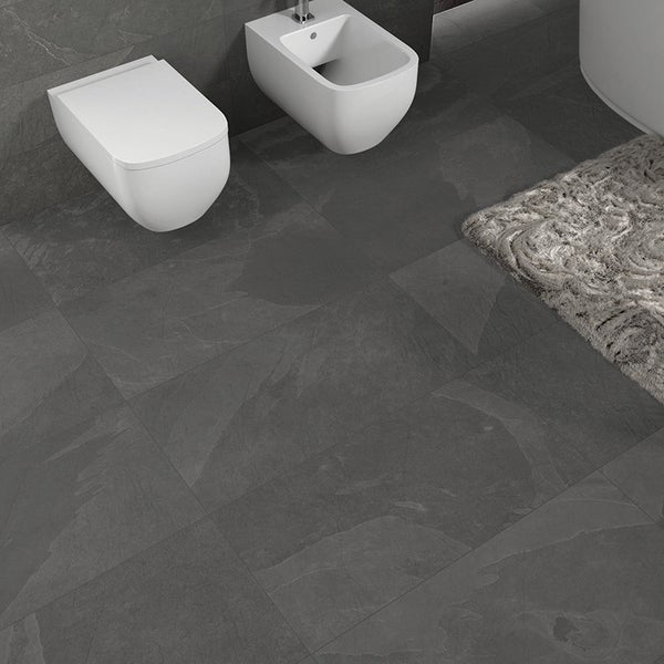 Badezimmer mit Wandfliesen und Bodenfliesen in Steinoptik, wandhängende Toilette und Bidet vor gefliester Wand mit Badematte.