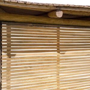 Sichtschutz aus waagerechten Holzlamellen unter einer Dachkonstruktion aus Rundholz.