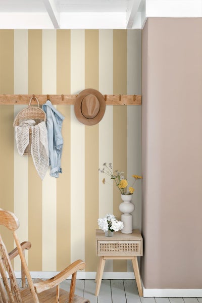 Vliestapete mit breiten vertikalen Streifen in Beige und Creme in einem hellen Raum mit Holzmöbeln und einer Garderobenleiste.