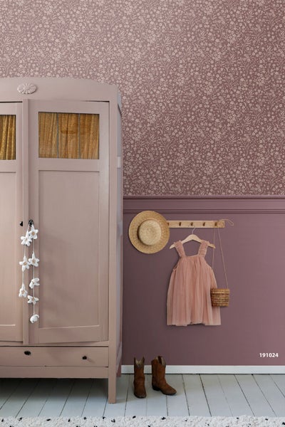 Kinderzimmer mit floraler Tapete, einem Holzschrank, einer Hakenleiste mit Hut und Kleid sowie Stiefeln auf dem Boden.