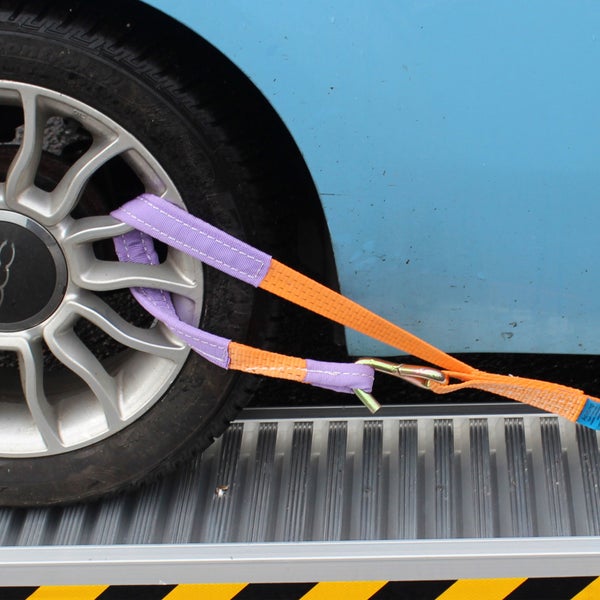 Ein Radsicherungsgurt mit Haken fixiert einen Autoreifen auf einer Auffahrrampe zur Ladungssicherung beim Transport.