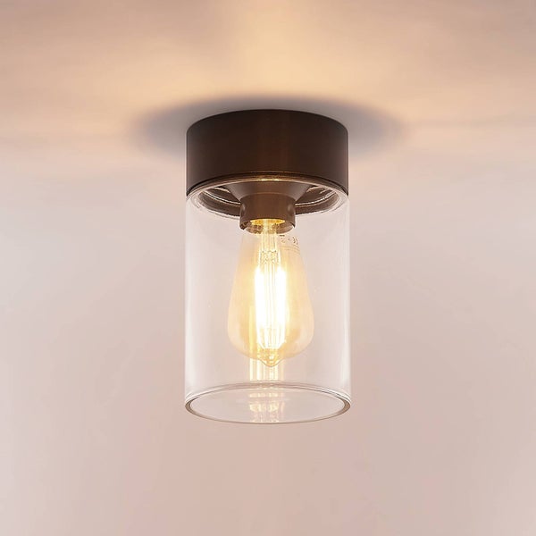 Zylindrische Deckenleuchte mit schwarzer Metallhalterung und klarem Glasschirm inklusive eingeschaltetem Leuchtmittel.