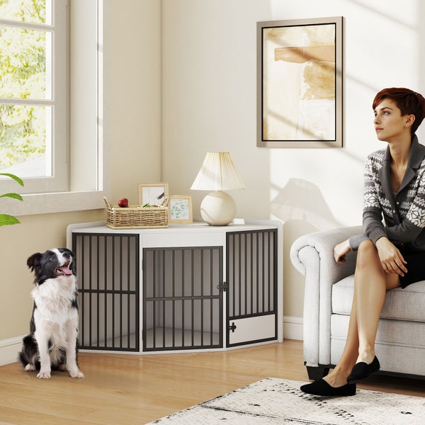 Eck-Hundekäfig aus Holz und Metall in Weiß und Schwarz, genutzt als Beistelltisch in einem hellen Wohnzimmer mit Hund und Person.