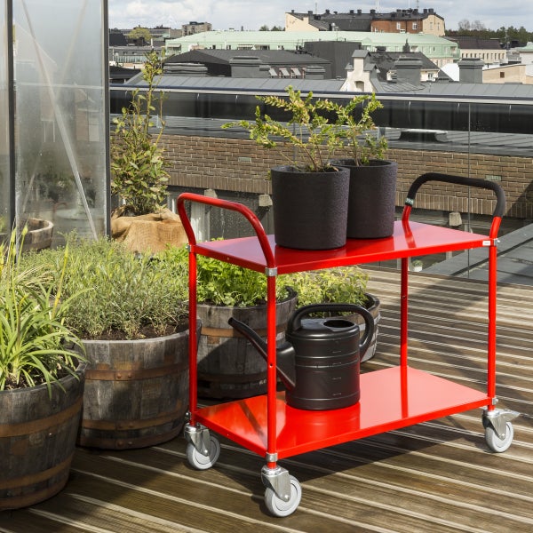 Roter Servierwagen mit Pflanzen und Gießkanne auf einer Dachterrasse