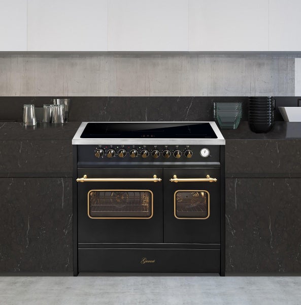 Freistehender Gurari Induktionsherd im Landhausstil mit zwei Backöfen und goldfarbenen Bedienelementen in moderner Küche mit dunkler Arbeitsplatte.