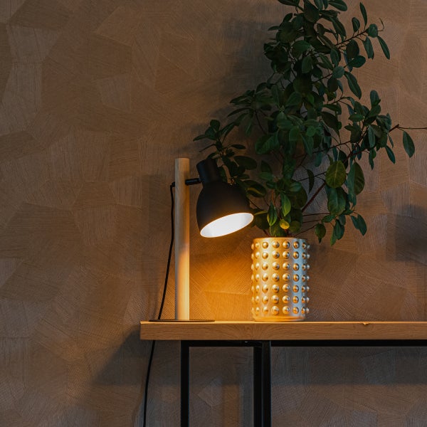 Tischleuchte mit Holzstandfuß und Pflanze in einem strukturiertem Blumentopf auf einem Konsolentisch vor einer gemusterten Tapete.