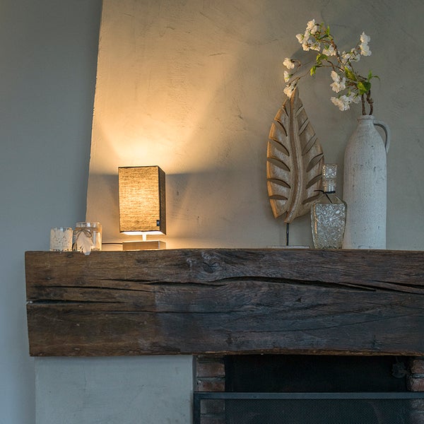 Dekorative Szene mit Tischleuchte, Kerzen, Vase und Holzornament auf einem Holzbalken