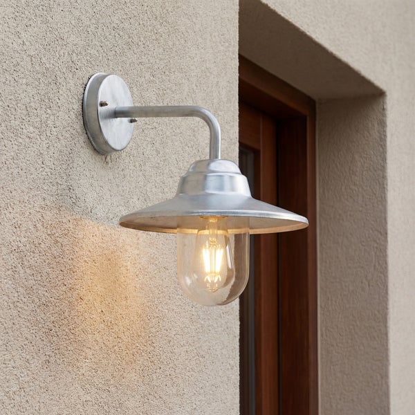Moderne Außenwandleuchte aus Metall mit klarer Glasabdeckung und warmweißem LED Leuchtmittel montiert an einer hellen Fassade.