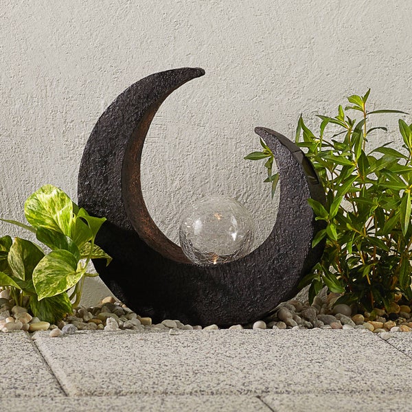 Mondsichel-Solarleuchte mit Glaskugel in Bruchglas-Optik auf Kieselsteinen neben Pflanzen.