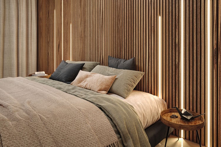 Modernes Schlafzimmer mit einer Wandgestaltung aus Holzlamellen und integrierter LED-Beleuchtung. Bett mit Kissen und rundem Beistelltisch.