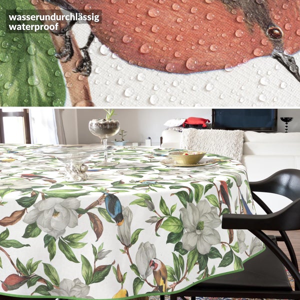 Runde, wasserfeste Tischdecke mit floralem Vogelmuster in hellem, modernem Zimmer; Detail zeigt Wassertropfen auf dem Stoff.