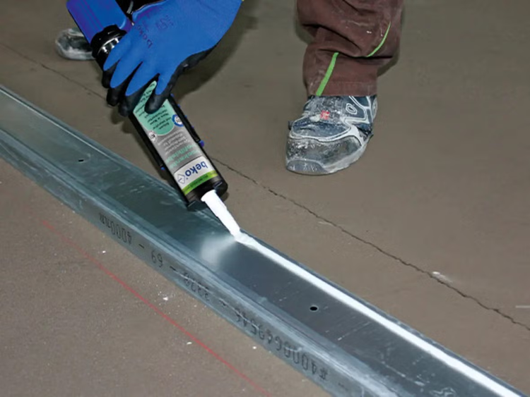 Handwerker appliziert mit einer Beko Kartuschenpistole Dichtstoff auf ein Metallprofil für Trockenbauarbeiten auf dem Boden