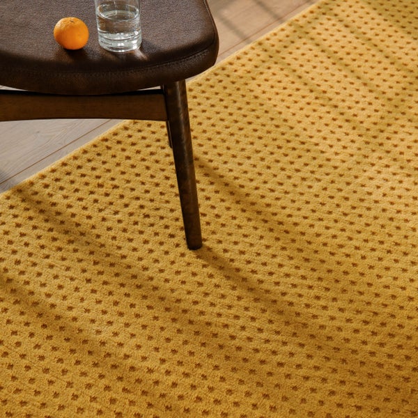 Strukturierter Teppich mit Punktmuster auf Holzboden neben einem Hocker.