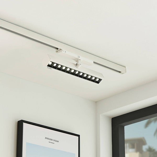 Weißer linearer LED Schienenstrahler montiert an einem Schienensystem an der Decke eines hellen, modernen Raumes.