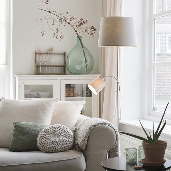 Wohnzimmer mit Sofa, Stehlampe und dekorativen Elementen auf einem Schrank