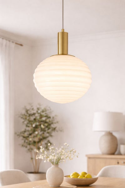 Moderne Pendelleuchte mit weißem, geriffeltem Glasschirm und messingfarbener Fassung in einem hellen Wohnraum.