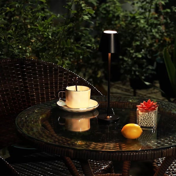 Szene mit einer Tischleuchte, einer Tasse Kaffee, einer Zitrone und einer Sukkulente auf einem Gartentisch.