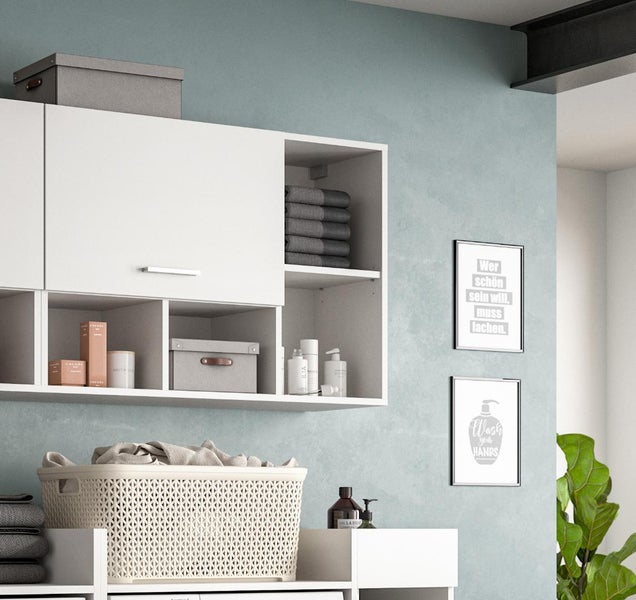 Moderner weißer Wandschrank mit offenen Fächern und Tür, organisiert mit Handtüchern und Boxen in einer hellen Waschküche.