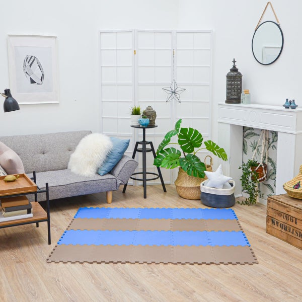 Helles, organisiertes Wohnzimmer mit grauem Sofa, weißem Paravent und einer blau-braunen Schaumstoff-Puzzlematte auf einem Holzboden mit Pflanzen.