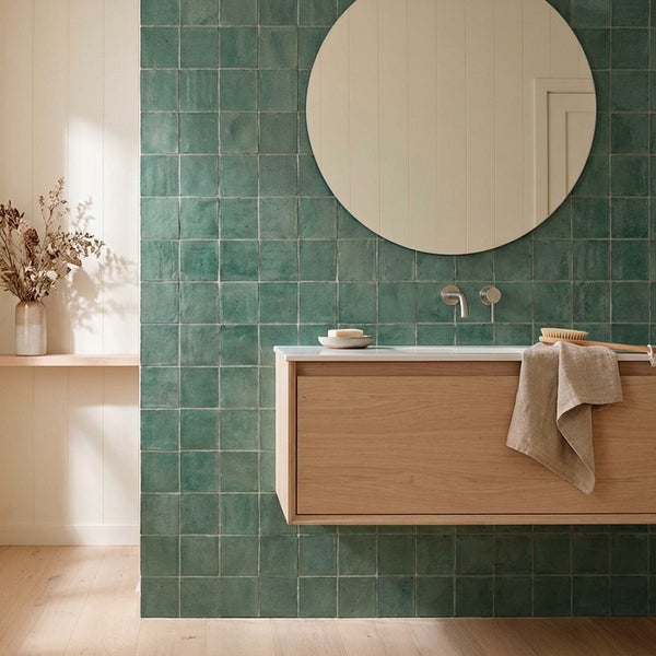 Modernes Badezimmer mit quadratischen Wandfliesen, Waschtisch aus Holz und rundem Spiegel.