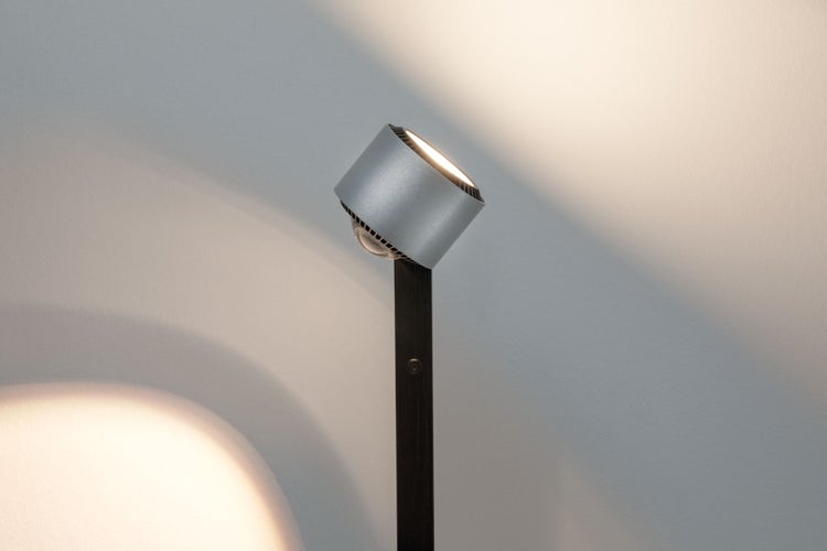 Moderne Stehleuchte mit verstellbarem Strahler aus gebürstetem Aluminium auf einem Standrohr, Lichtkegel an der Wand.