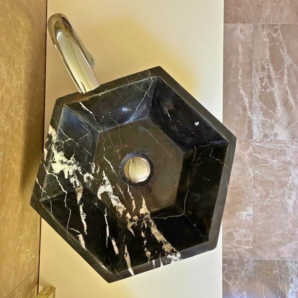 Sechseckiges Aufsatzwaschbecken aus gemasertem Marmor mit einer verchromten Armatur in einem hellen, modernen Badezimmer.