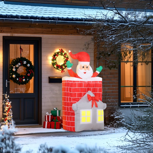 Aufblasbare Weihnachtsfigur Weihnachtsmann im Schornstein auf einem Haus, beleuchtet, Außenbereich mit Schnee, Haustür, Kranz und Geschenken.