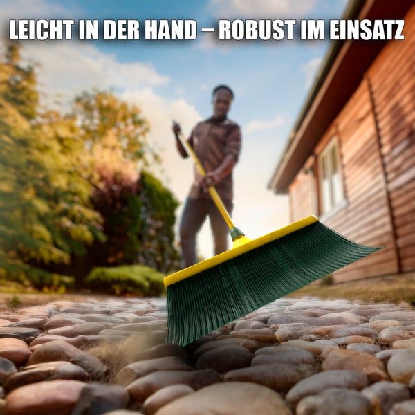 Besen mit gelbem Stiel und dunklen Borsten beim Fegen eines steinigen Weges
