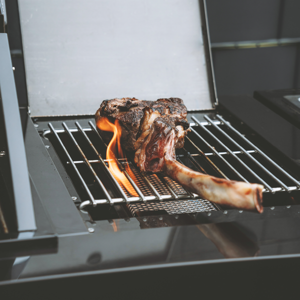 Ein Tomahawk-Steak wird auf einem Gasgrill über einer offenen Flamme zubereitet.