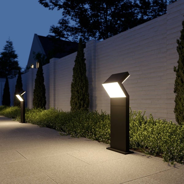 Moderne schwarze LED-Wegleuchten beleuchten einen gepflasterten Gartenweg bei Nacht vor einer weißen Ziegelmauer und Hecken.