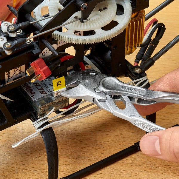 Eine Hand hält eine Knipex Zange an einem elektronischen Bauteil eines Helikopters.
