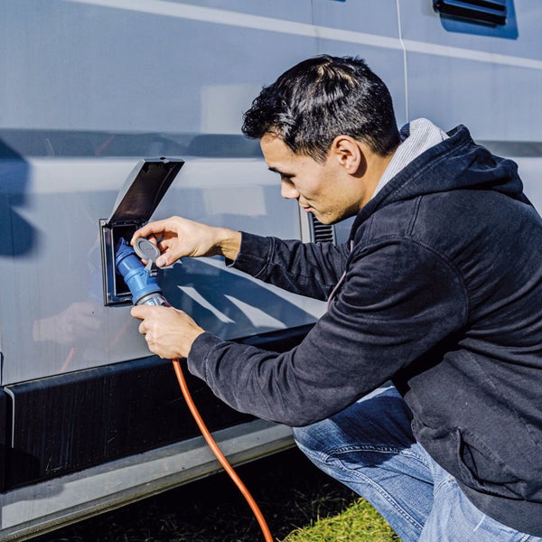 Eine Person schließt ein Stromkabel an einen Campingwagen an.