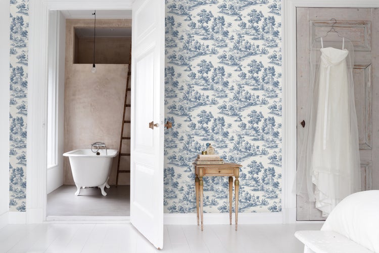 Helles Zimmer mit Toile-de-Jouy-Tapete, hölzernem Beistelltisch und Blick auf eine freistehende Badewanne durch eine offene Tür.