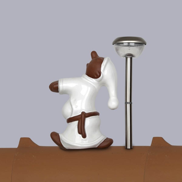 Gartenfigur Schlafwandler als Dachschmuck aus weißer Keramik mit einer silbernen Solar-Gartenleuchte auf einem braunen Firstziegel.