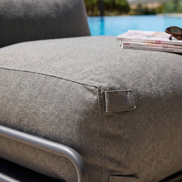 Detailansicht eines grauen Outdoor-Loungekissens aus strukturiertem Stoff auf einem Metallrahmen im Außenbereich neben einem Pool.