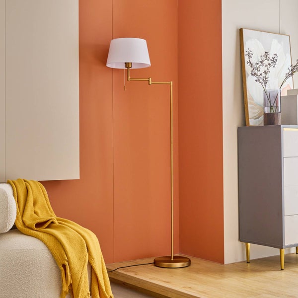 Goldene Stehlampe mit weißem Lampenschirm neben einem beigen Sessel mit gelbem Überwurf