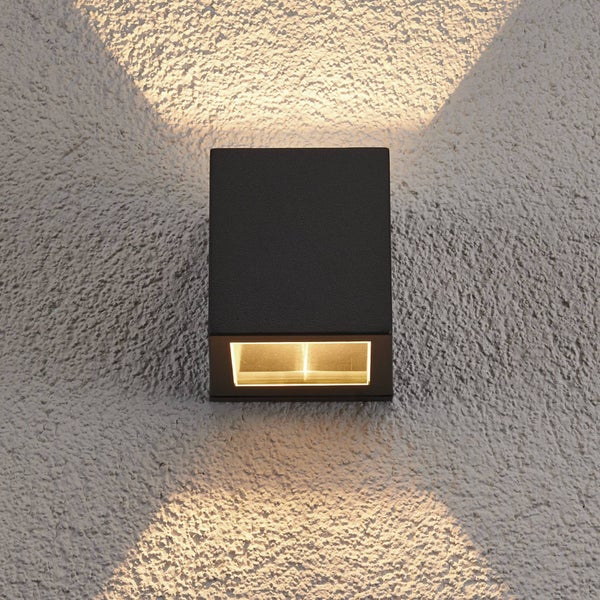 Quadratische schwarze Außenwandleuchte mit Lichtaustritt nach oben und unten auf einer strukturierten Wand.