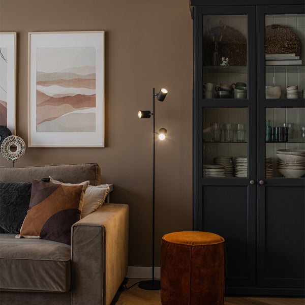 Wohnzimmer mit Sofa, Stehlampe, Hocker und Vitrinenschrank