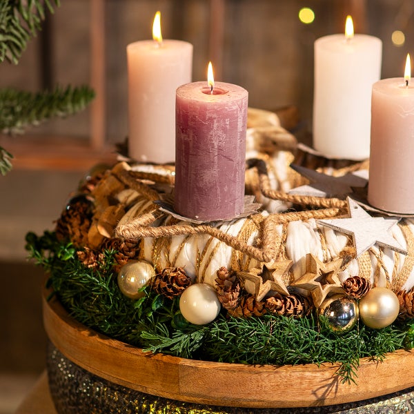Adventskranz mit vier brennenden Stumpenkerzen, Tannenzweigen, Kugeln und Sternen auf einem Holzteller