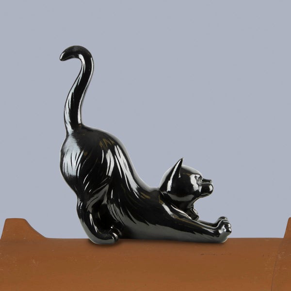 Firstfigur Katze aus Keramik, glänzend schwarz, in streckender Pose auf einem Firstziegel.