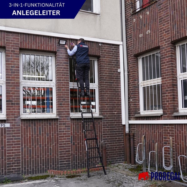 Ein Mann steht auf einer Anlegeleiter vor einem Gebäude und montiert eine Lampe.