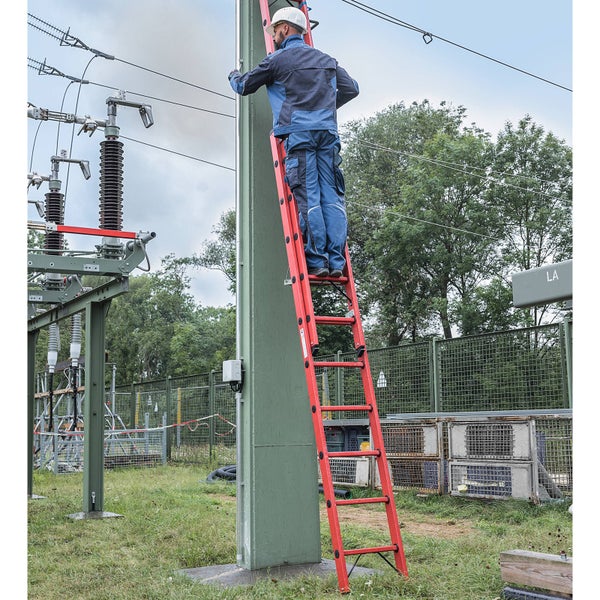 Eine Person mit Schutzhelm und Arbeitskleidung steht auf einer roten Leiter, um an einem Strommast zu arbeiten.